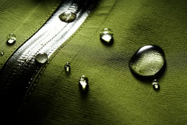 Gocce d'acqua su tessuto verde, dimostrando il significato di "water repellent".